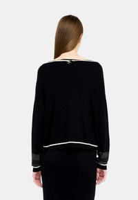 Maglione nero in maglia con maniche lunghe, caratterizzato da bordi bianchi sul collo e sui polsini, e maniche decorate con piccoli strass.
