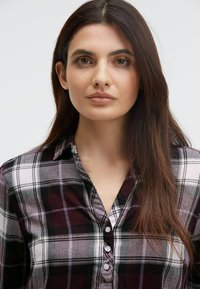 Plaid button-up shirt in dark red, white, and black. Features a collared neckline and long sleeves with a smooth, soft texture.