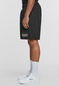 Sorte mesh basketball-shorts med snor i livet, med hvit tekst "New York City Basketball". Brukt med hvite sneakers og knelange sokker.