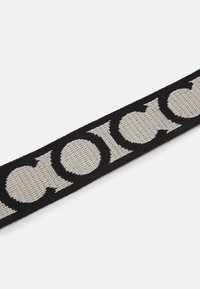 Pasek z tkaniny o czarnej bazie z dużymi beżowymi literami ułożonymi w odważny, powtarzający się wzór. Miękka faktura, trwały materiał.