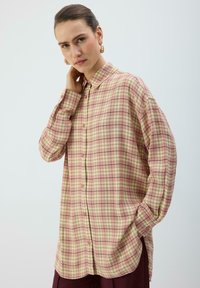 Chemise à manches longues à boutons, motif à carreaux rose, crème et vert. Elle présente un col et des fentes latérales, confectionnée dans un tissu léger.