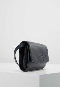 Kožená kabelka v námořnické modré, s texturovaným povrchem, klopovým uzávěrem a boční rukojetí pro snadné nošení. Kompaktní design.