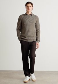 Suéter marrón de canalé, pantalones negros y zapatillas blancas. El suéter tiene un cuello redondo, mientras que los pantalones tienen un corte recto.