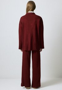 Burgundy knit suit consisting of a loose-fitting blazer and wide-leg pants. Smooth texture; minimalistic design; no visible hardware or patterns.