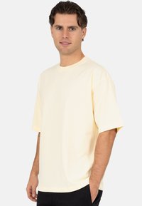 T-shirt met korte mouwen en ronde hals in een zachte pastelgele kleur, gemaakt van gladde stof. Heeft een ontspannen pasvorm en een rechte zoom.