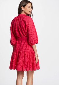 Vestido rosa de volantes hecho de encaje de ojo de perdiz, con cintura ajustada y espalda fruncida. Presenta mangas abullonadas y detalles de dobladillo en forma de concha.