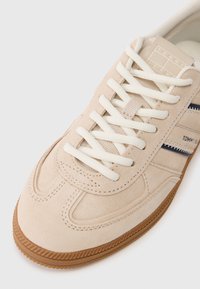 Μπεζ σουέτ αθλητικά παπούτσια με κρέμ κορδόνια, υφασμάτι νες λεπτομέρειες και σκούρες μπλε ρίγες. Διαθέτουν υφασμάτινη σόλα από καουτσούκ και μια διακριτική λεπτομέρεια λογότυπου.