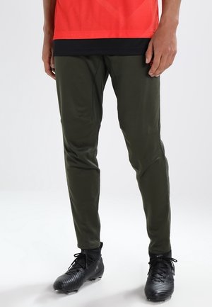 Olive green athletic pants made of smooth, flexible fabric with a tapered design and subtle seams, paired with black soccer shoes.