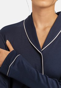 Maglia da pigiama blu navy con maniche lunghe, caratterizzata da un colletto e bordi delle maniche bianchi. Materiale morbido con una texture liscia.