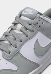 Baskets Nike blanches et grises avec des lacets gris, un logo swoosh cousu et une languette en tissu de marque.