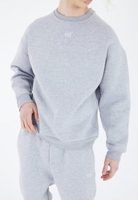 Grauer Pullover mit gerippten Bündchen und Saum, strukturiertem Stoff und subtilen Logodetails auf der Brust, kombiniert mit passenden grauen Sweatpants.