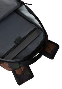 Wnętrze plecaka w wzór kamuflażu z szarym wykończeniem, z poduszkowaną przegródką na urządzenie i czarnym zamknięciem na zamek.