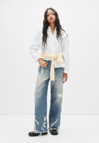 Hvid button-up skjorte, lysegul sweater bundet om taljen, slidte vidde jeans i blå med malingspletter, sorte sko.