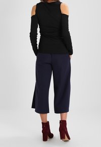Black long-sleeve top with shoulder cutouts, paired with navy wide-leg trousers. Burgundy ankle boots complete the outfit.