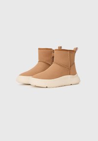 Botas de tobillo marrones hechas de un material suave parecido al ante, con una suela de goma crema de textura estriada y un zipper lateral para facilitar su uso.