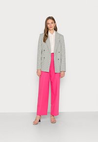 Blazer de xadrez duplo em cinza e branco, combinado com calças largas rosa-choque de cintura alta. Saltos transparentes realçam o visual.