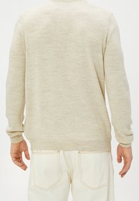 Beige svetr s měkkou texturou, kulatým výstřihem a ribovanými manžetami. V kombinaci s bílými džíny vyrobenými z denimu, které mají zadní kapsy a oranžové švy.