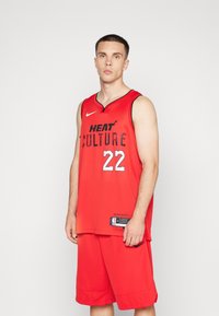 Camiseta de baloncesto roja con el texto "HEAT CULTURE" y el número 22. Presenta el logo de Nike, diseño sin mangas y textura transpirable. Combinada con pantalones cortos a juego.