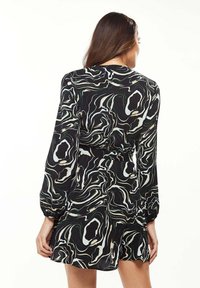Black dress with abstract green and cream swirl pattern, long sleeves, cinched waist, and a flared hem. Smooth fabric, mid-thigh length.