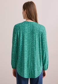 Blouse verte à manches longues avec un motif abstrait texturé, dotée d'un col rond et d'un ourlet arrondi, fabriquée en tissu léger.