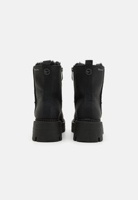 Botas negras hasta el tobillo con un exterior texturizado, cierre de cremallera y forro suave. Suelas de goma negras gruesas con acentos estriados para mayor tracción.