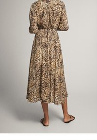 Sukienka midi w wzór lamparta, wykonana z lekkiego materiału, z długimi rękawami, wcięciem w talii oraz zwiewnym dołem w warstwowym fasonie.