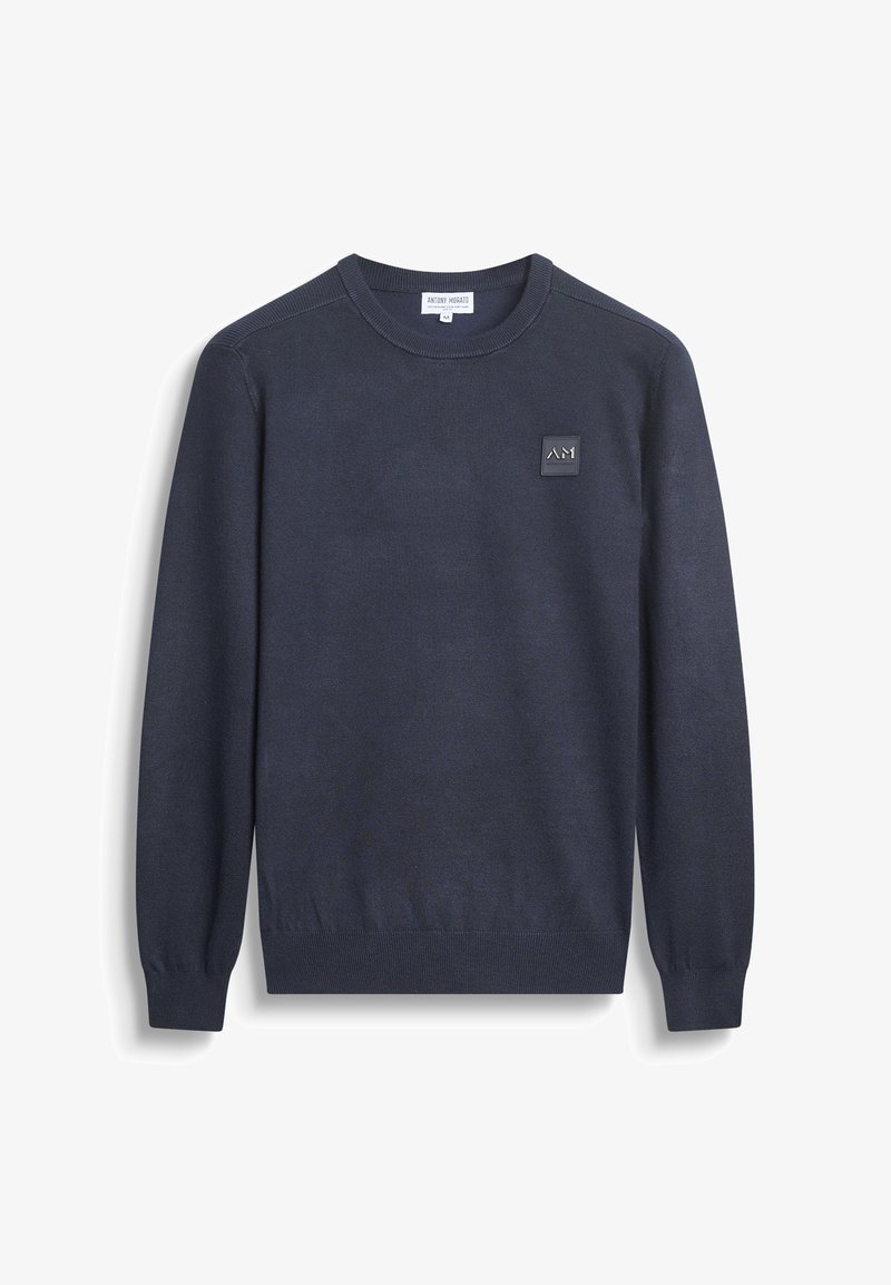 Navy plavi pleteni džemper s rebrastim manšetama i rubom, s kvadratnim logotipom na prsima. Klasični dizajn s okruglim izrezom, glatke teksture.