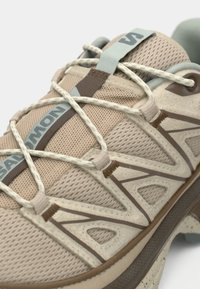 Αθλητικό παπούτσι ανοιχτού μπεζ χρώματος με επάνω μέρος από δίχτυ και καφέ λεπτομέρειες. Διαθέτει λαστιχένια σόλα και ελαστικό σύστημα κορδονιών για ασφαλή εφαρμογή.