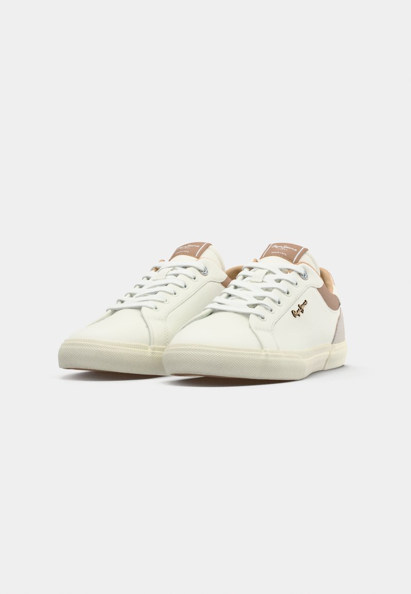 Par de zapatillas blancas de caña baja con acentos beiges, cordones blancos y logo de la marca en el lateral, exhibidas sobre un fondo blanco.