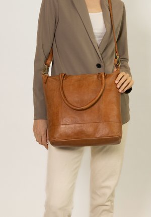 Brown leather tote bag with dual top handles and a detachable shoulder strap. Features a structured design and visible stitching details.