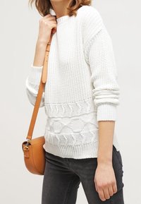 Biały dzianinowy sweter z fakturowanym wzorem, z opuszczanymi ramionami i ściągaczami na mankietach, zestawiony z małą beżową torebką na ramię.