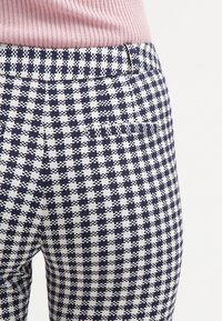 Navy and white checkered patterned pants, featuring a textured fabric, fitted design, and a belt loop at the waist.
