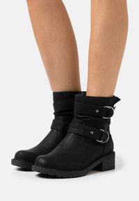 Botas negras hasta el tobillo de cuero sintético con dos correas ajustables y hebillas plateadas. Tacón plano y suela texturizada para mayor agarre.