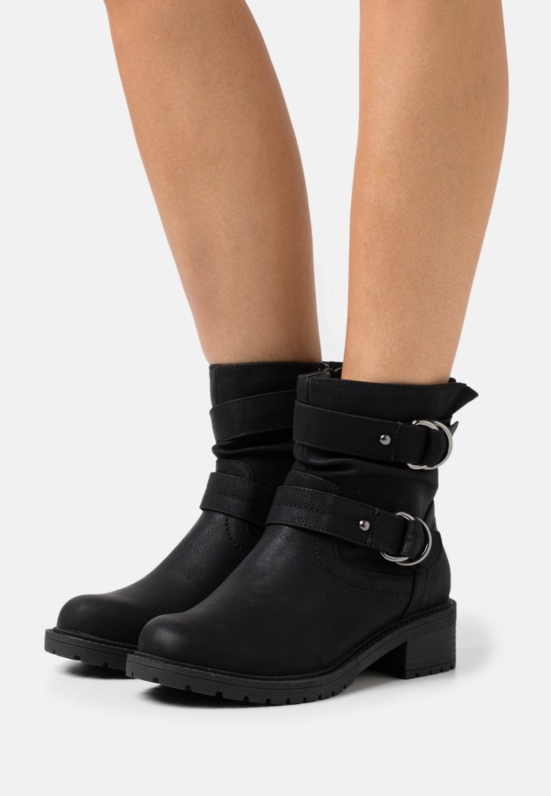 Botas negras hasta el tobillo de cuero sintético con dos correas ajustables y hebillas plateadas. Tacón plano y suela texturizada para mayor agarre.