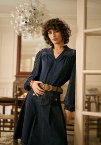 Blouse bleu marine à manches en dentelle, associée à une jupe en denim foncé avec une taille ceinturée et des boutons décoratifs. Design simple et élégant.