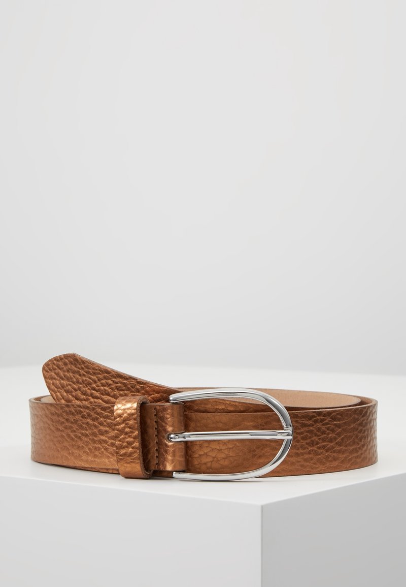 Ceinture en cuir marron texturé avec boucle en métal argenté arrondie posée sur une surface blanche inclinée.