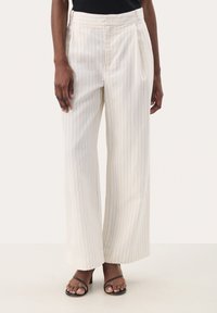 Pantalon à jambes larges crème avec fines rayures verticales, confectionné dans un tissu lisse. Présente des plis et une taille haute. Assorti à des sandales à talons noires.