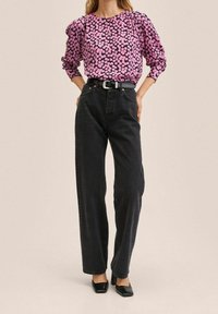 Lilla bluse med sort blomsterprint, puffede ærmer, parret med højtaljede sorte jeans og sorte firkantede hæle.