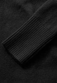 Svart ulltröja med ribbad mudd och ett mjukt, texturerat kropp. Tyget verkar jämnt med lätt fleece-detalj.