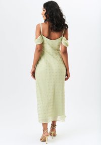 Mint green dress with a fitted silhouette, decorative gold dots, off-shoulder sleeves, and a mid-calf length, paired with gold heeled sandals.