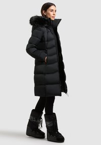 Svart vadderad jacka med huva kantad med päls, med quiltad design, dragkedja framtill och sidofickor. Matchas med svarta isolerade stövlar.