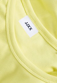 Ljusgul ribbad linne med rundad halsringning; har en vit etikett med svart text "JJXX" på insidan av kragen. Mjuk textur.