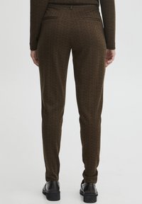 Brown herringbone patterned trousers with a tapered fit, featuring two back pockets and a concealed waistband. Textured fabric with subtle sheen.