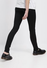 Jeans skinny negros hechos de una tela elástica, con una textura suave y un ajuste ceñido, combinados con zapatos negros con cordones.