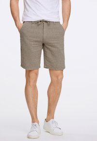 Pantalones cortos de mezcla de lino color arena con una sutil textura a rayas, cintura elástica, cierre con cordón y bolsillos laterales. Usados con zapatillas blancas.
