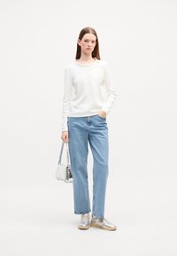 Witte lange mouwen top, lichtblauwe rechte spijkerbroek, zilveren sneakers en een kleine zilveren handtas met een gestructureerde afwerking.