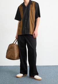 Koszula z krótkim rękawem w czarne i brązowe pionowe paski, w połączeniu z luźnymi czarnymi spodniami i białymi trampkami. Brązowa skórzana torba z paskiem.