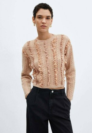 Pull en tricot rose avec des accents volants, des manches longues et un col rond, associé à un pantalon noir taille haute.