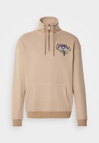 Beige sweatshirt with a high collar, half-zip front, large front pocket, and colorful floral embroidery on the left chest. Soft texture.