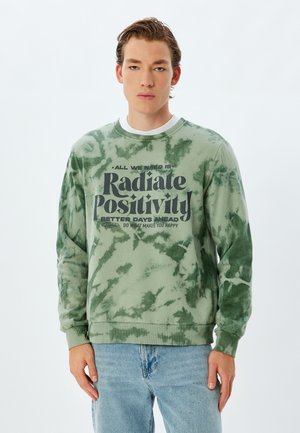 Grøn tie-dye sweatshirt lavet af bomuld, med lange ærmer, ribbet halsudskæring og fed trykt tekst på forsiden.